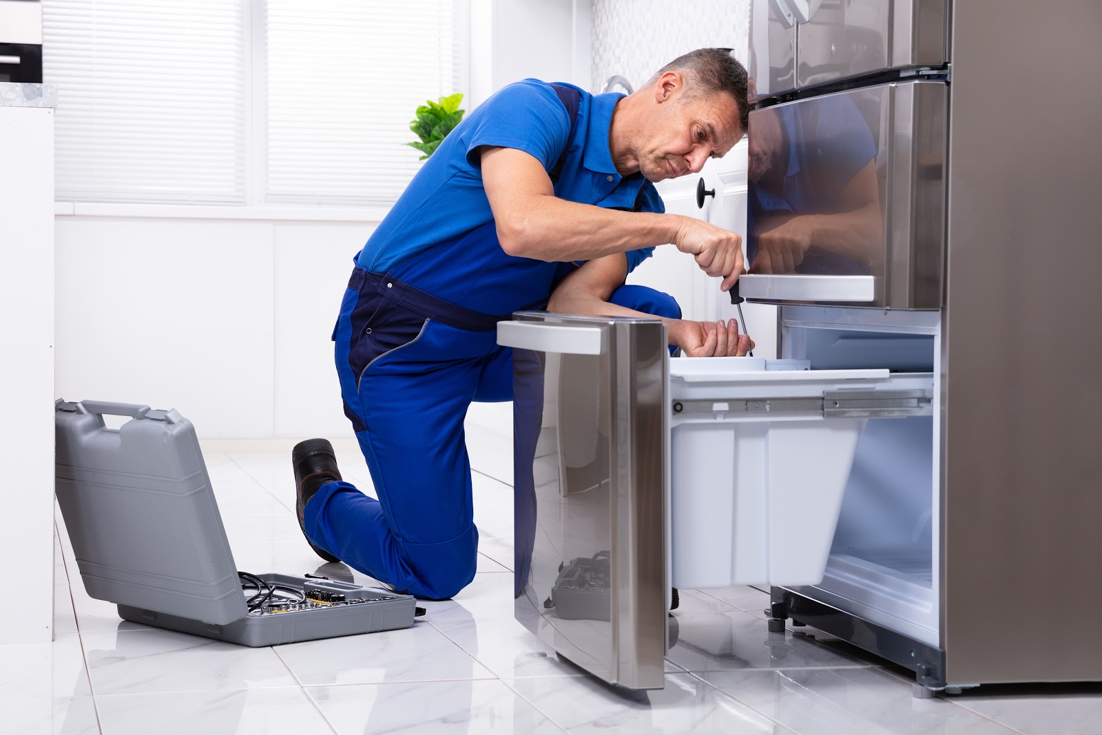 A technician repairing a dishwasher in a modern kitchen.