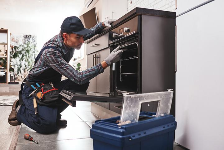 Technician repairing an oven in a kitchen.