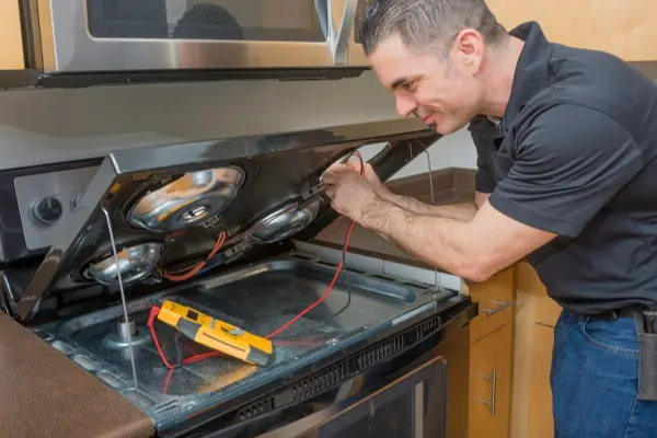 Technician repairing an oven with diagnostic tools.